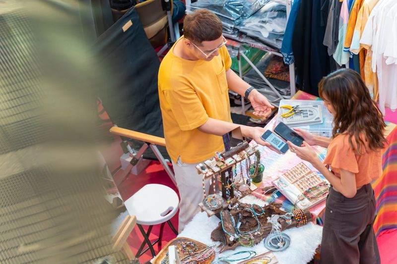 Customer buying handmade jewelry and using smartphone scan QR code for making online at shopping mall. Small business shop owner and contactless payment technology concept.