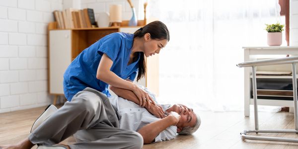 A nurse assisting an elderly man who has fallen on the floor.