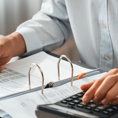 Person using a calculator with documents in a binder on a desk.