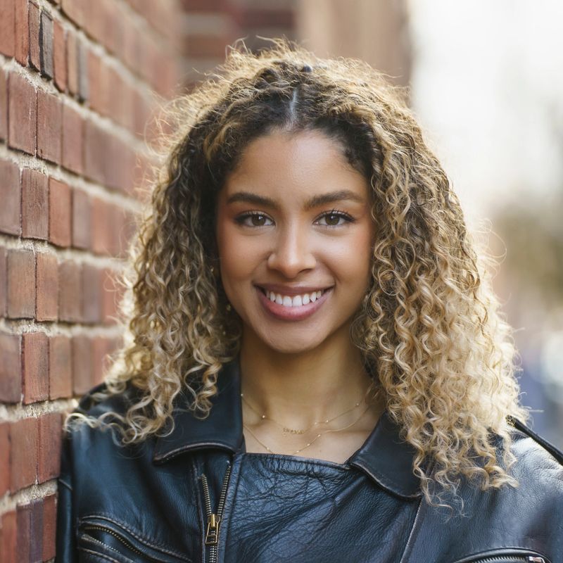 Close up portrait of a beautiful young woman with curly hair, smiling and looking at camera