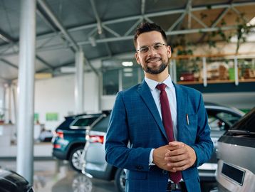 Confident man in a blue suit standing in a car showroom.