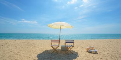 Two beach chairs under a white umbrella on a sunny sandy beach by the ocean.