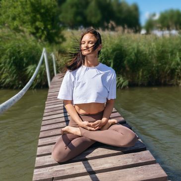 Woman meditating outdoors on a wooden bridge.