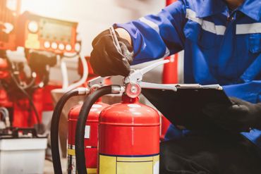 Technician inspecting fire extinguishers with clipboard in hand.