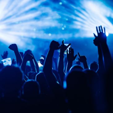 Crowd cheering and raising hands at a concert with blue stage lights.