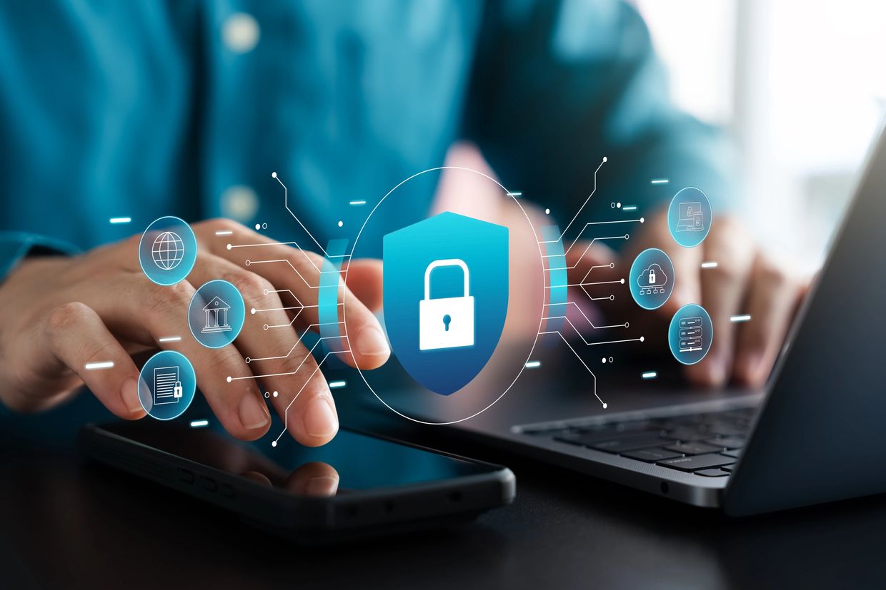 Person using smartphone and laptop with digital security icons overlay.