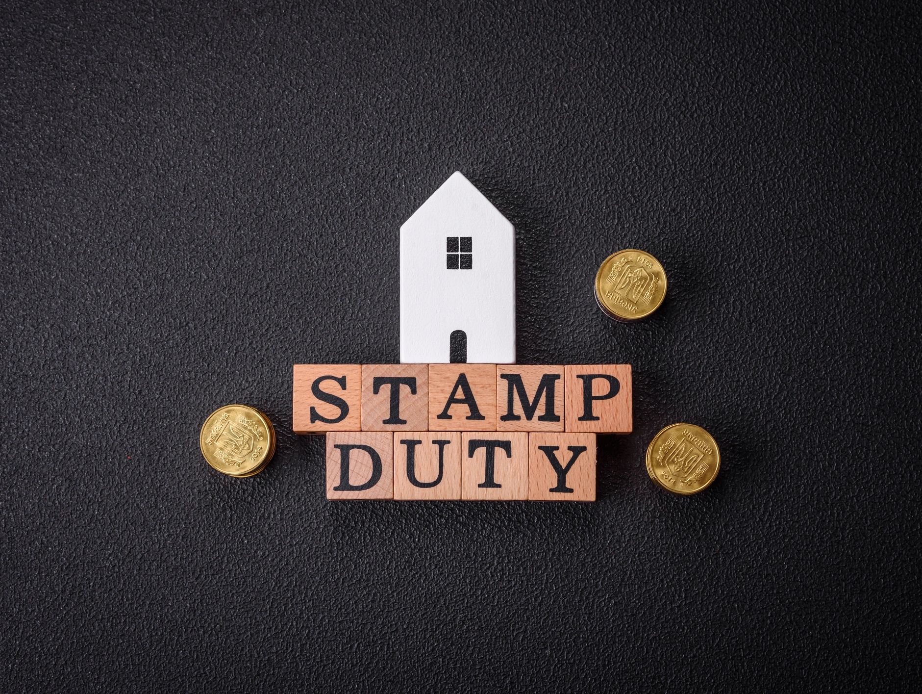 House model on “STAMP DUTY” blocks with coins on black background.