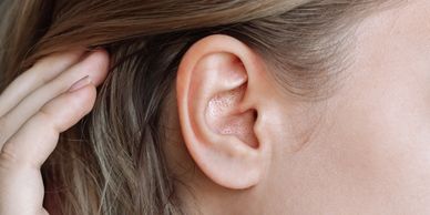 Close-up of a person's ear with hand touching hair.