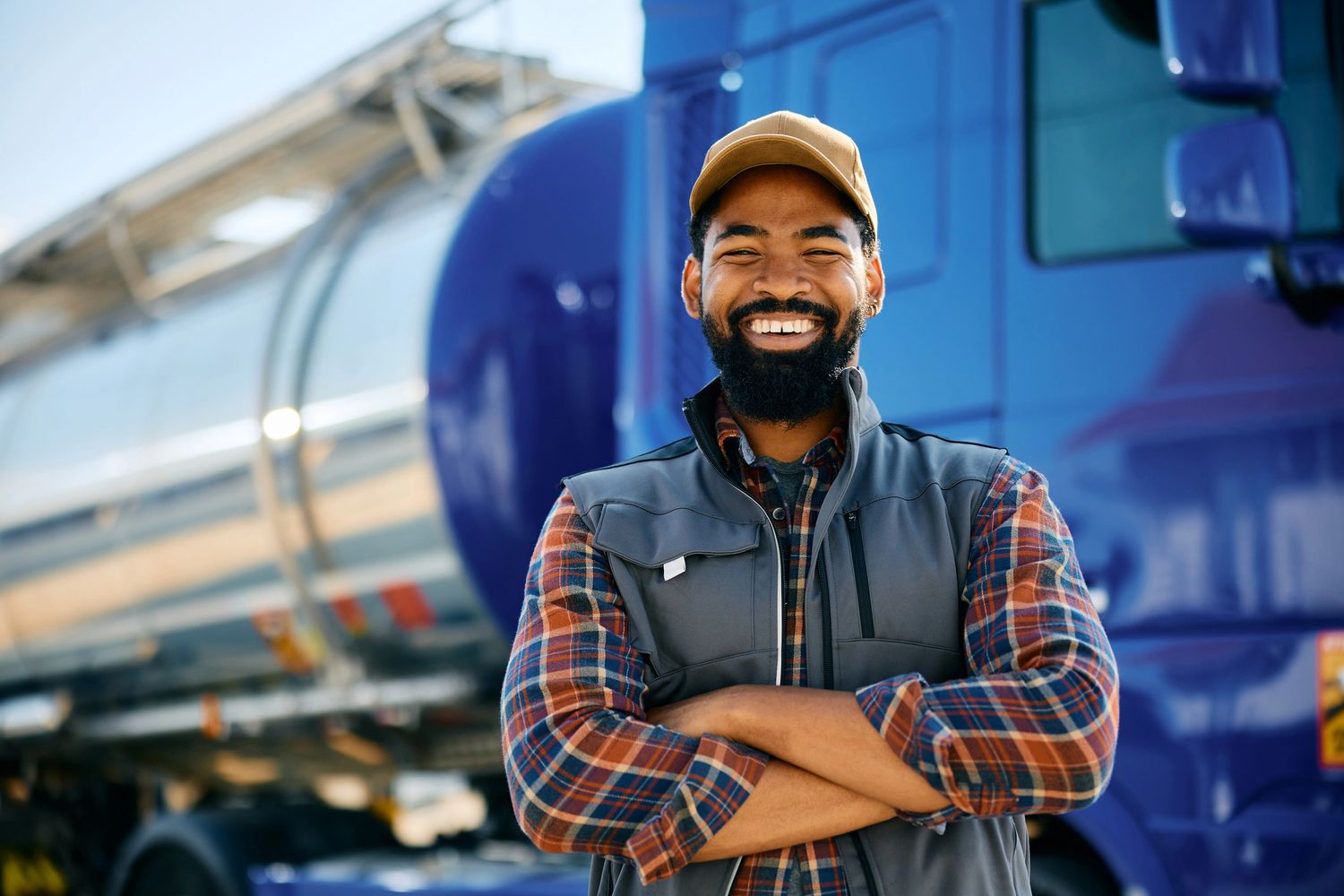Smiling truck driver standing confidently in front of his blue semi-truck.