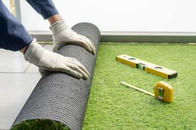 Hands rolling out artificial grass with measuring tools nearby.