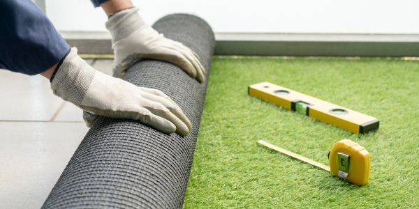 Person laying artificial turf with tools nearby.