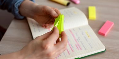 Hands holding a yellow sticky note over an open notebook with highlighted notes.