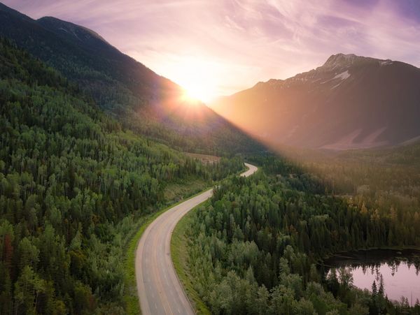 A winding road through a lush forest at sunset in the mountains.