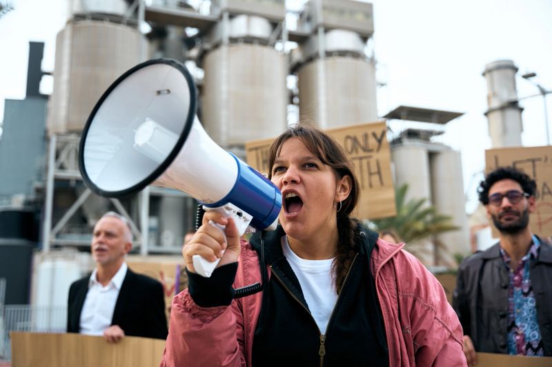 Angry and rebellious woman speaking and protesting with megaphone at demonstration at climate change and global warming. Group of activists people at a pro-earth manifestation with banners
