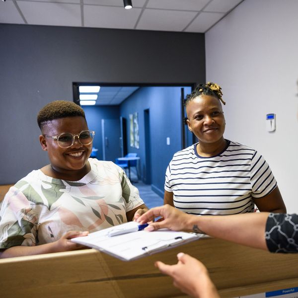 Two women smiling at a reception desk while receiving a clipboard.