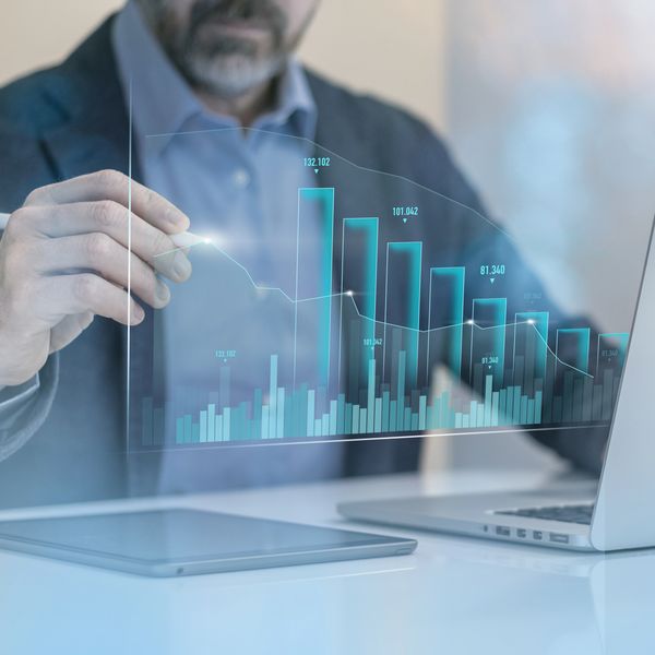 Man analyzing futuristic transparent digital bar graph data on a desk.