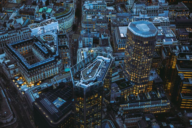 Aerial panoramic view of The City of London cityscape skyline with metropole financial district modern skyscrapers after sunset on night with illuminated buildings and cloudy sky in London, UK