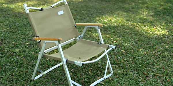 A beige folding chair with wooden armrests on grass.