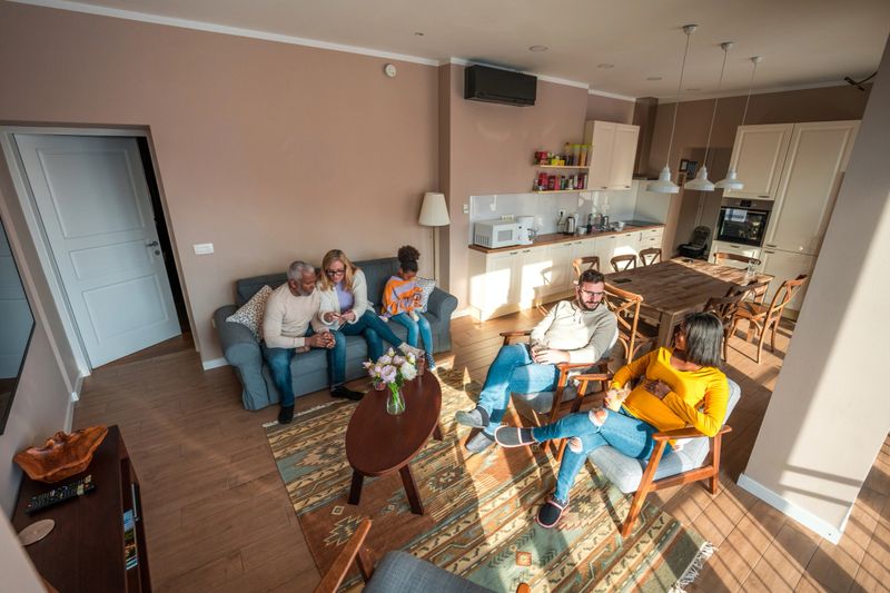 A diverse multigenerational family sits on a couch, engaged in knitting, with drinks on the coffee table in a cozy living room.