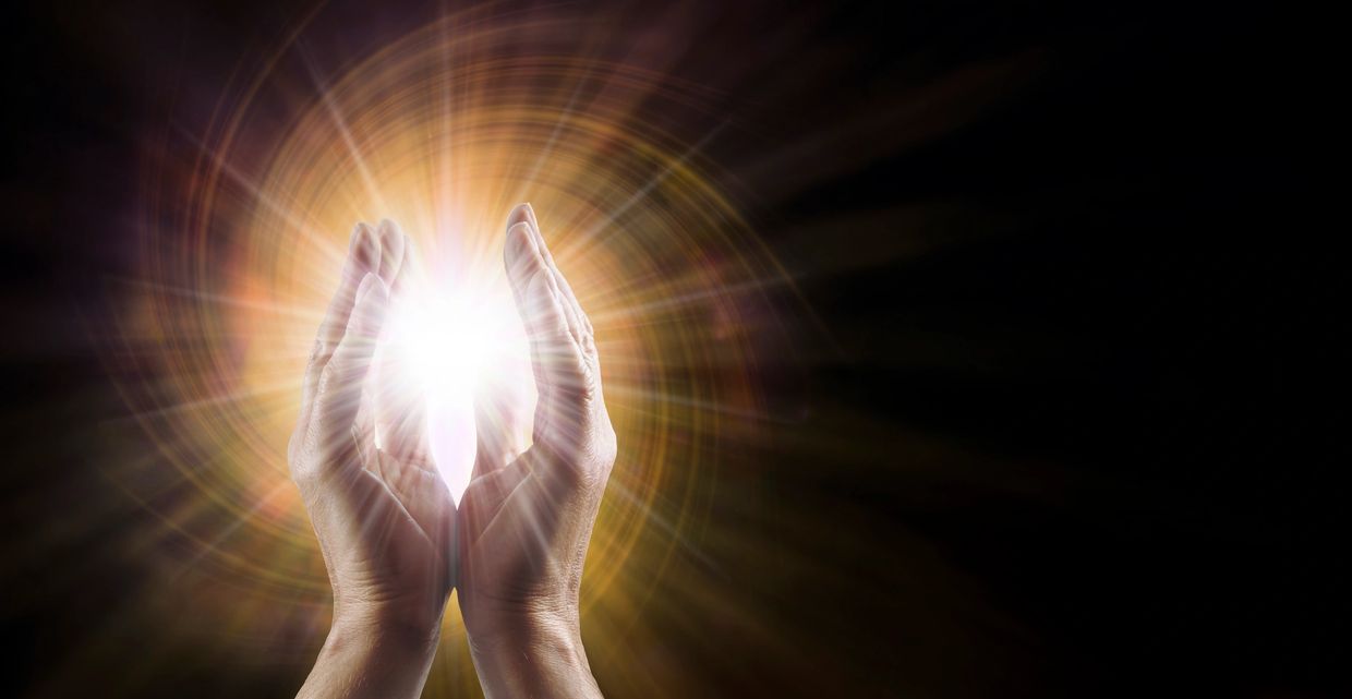 Hands holding bright glowing light with dark background.