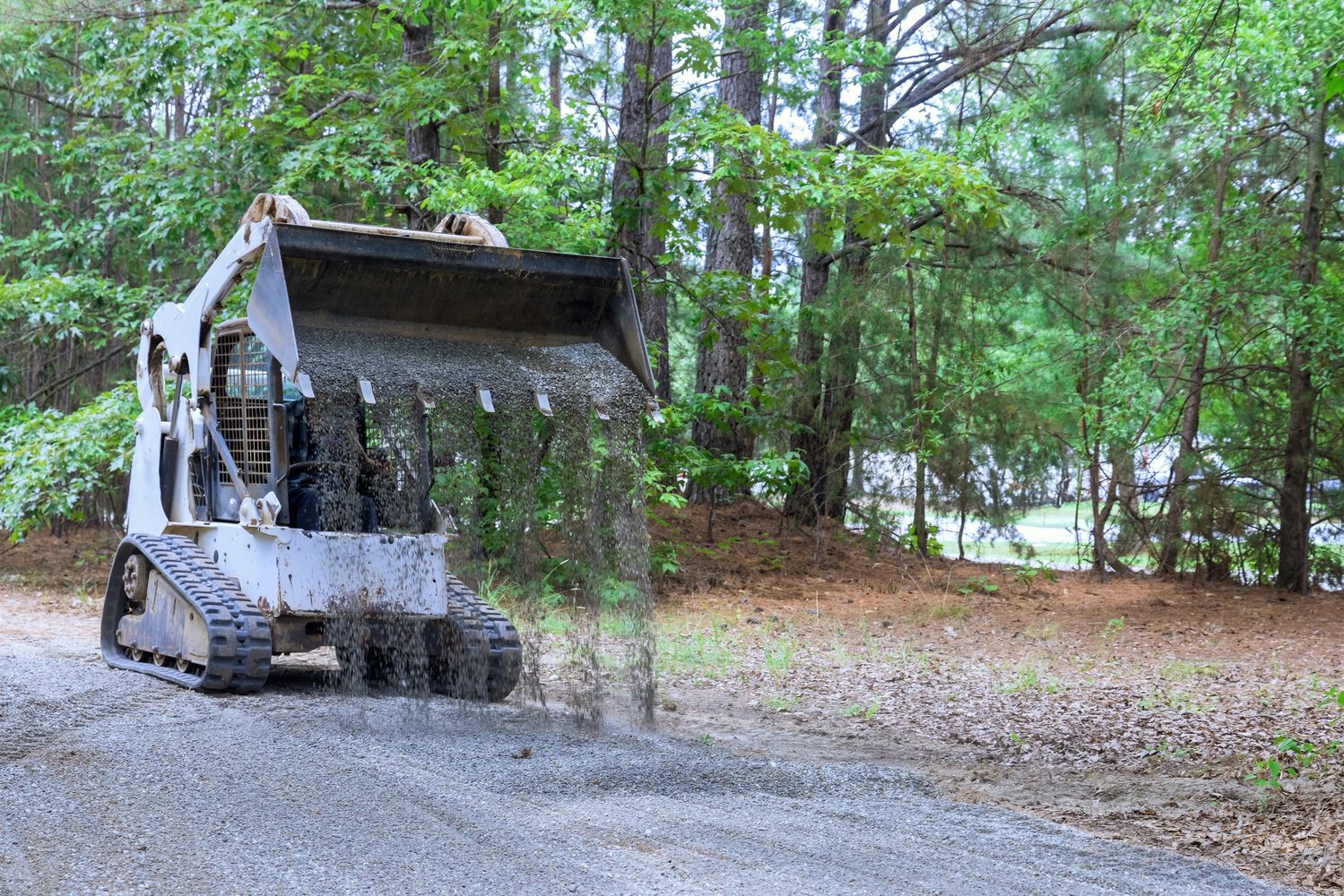 A skid-steer loader spreading gravel on a forest path.