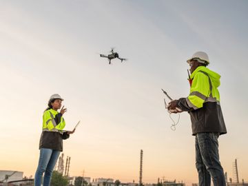 Two engineers operating a drone at a construction site during sunset.