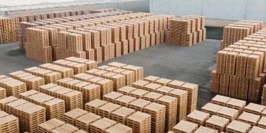Large stacks of wooden pallets arranged in an outdoor industrial area.