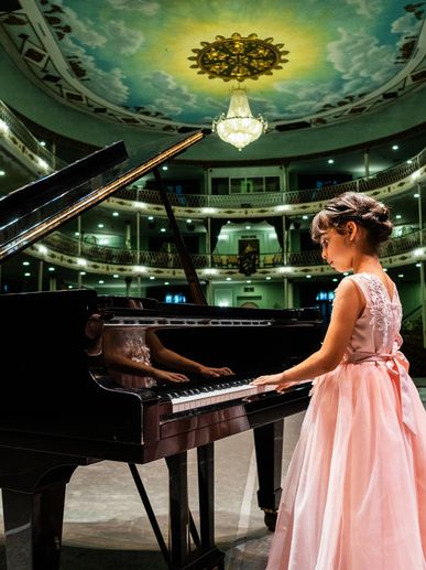 A young child in a pink dress is in a hall with a green ceiling and a lovely chandelier. She is play