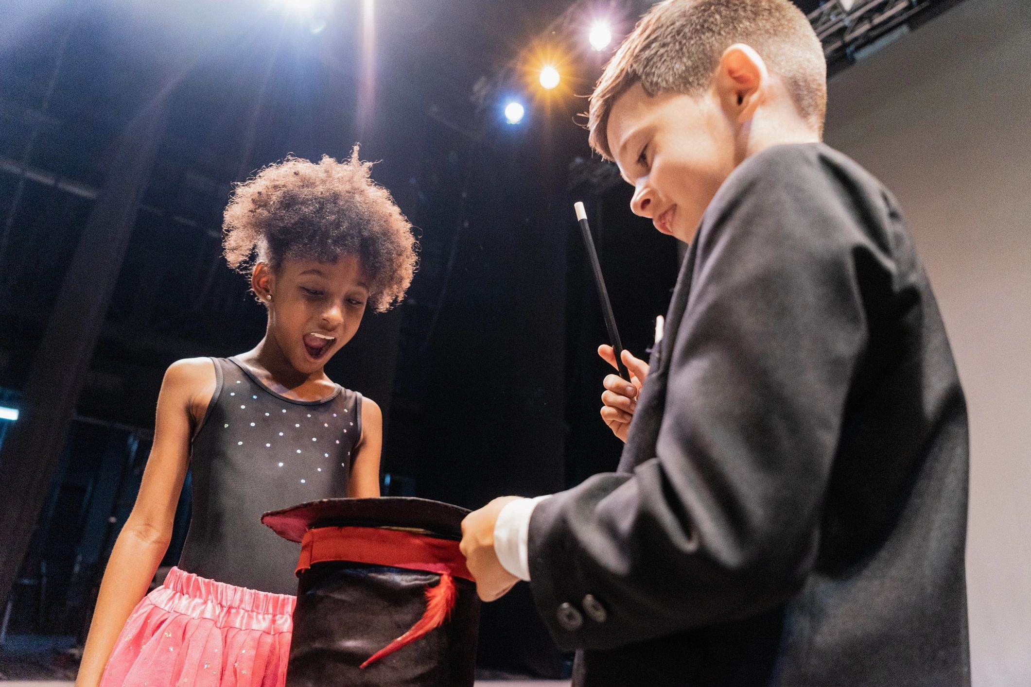 A magician amazes a young girl by pulling a surprise from a hat.