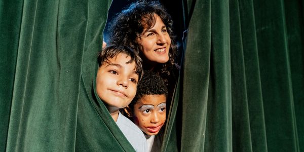 A woman and two children peeking through green stage curtains with excitement.