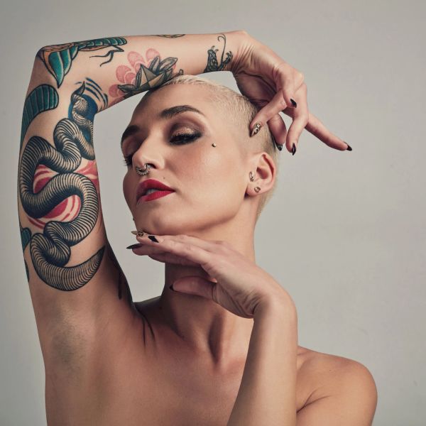 Person with tattoos posing with hands near face.