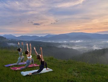 Three women practicing yoga on mats overlooking misty mountains at sunrise.