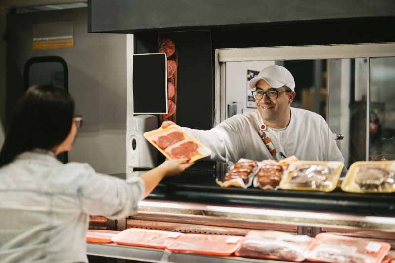 Friendly salesman working at the grocery shop handing a packet with fresh meat to female customer