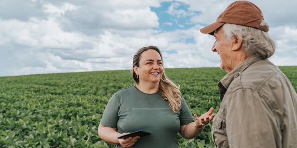 Two farmers discussing crops in a green field under a cloudy sky.