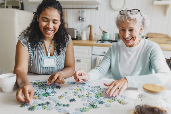 Two women happily assembling a puzzle together at a kitchen table.