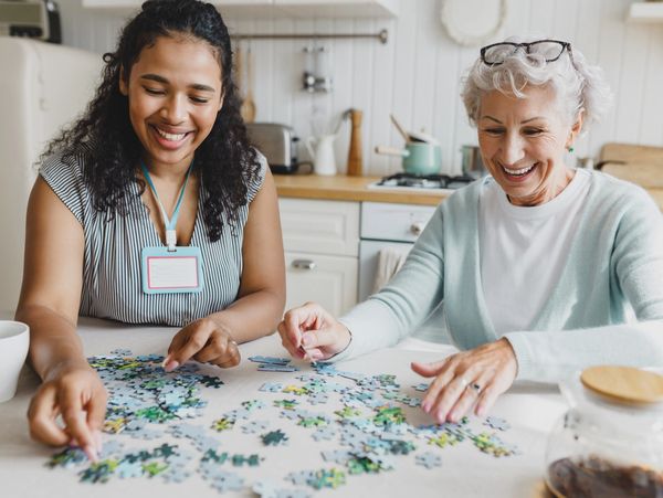 Two women happily assembling a puzzle together at a kitchen table.