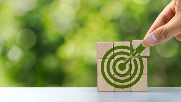 Hand placing a wooden block to complete a target with an arrow hitting the bullseye.