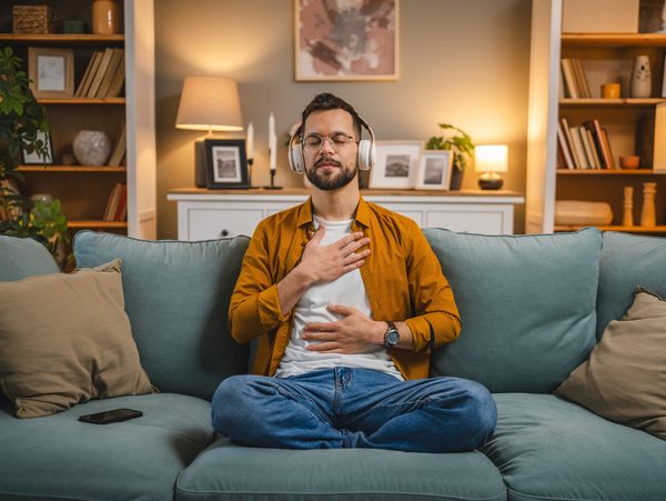 Man meditating on a couch with headphones in a cozy living room.