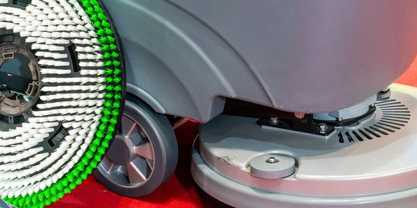 Close-up of an industrial floor cleaning machine with brushes and wheels.