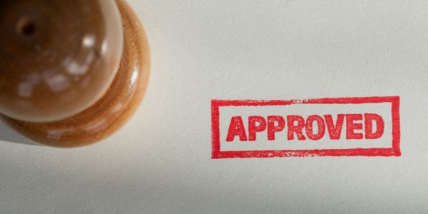 Wooden stamp with red approved mark on paper.