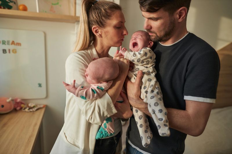 Mother and father are taking care of newborn baby twins. They are carrying them in the bedroom.
