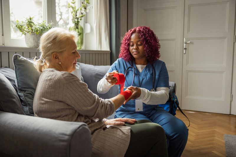 Nurse visiting mature patient at home. She is checking senior women's injured elbow.