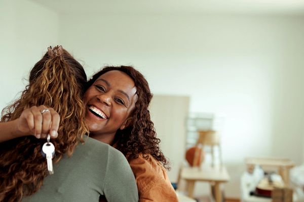 Two women hugging, one holding house keys, celebrating joyfully.