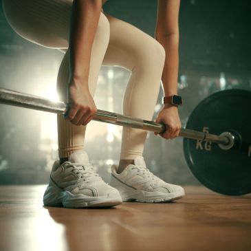 Person gripping a barbell, preparing to lift weights in a gym.