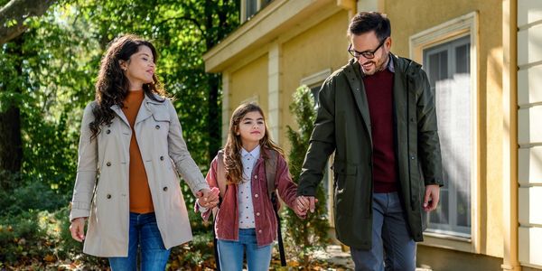 Parents holding hands with their daughter while walking outside.