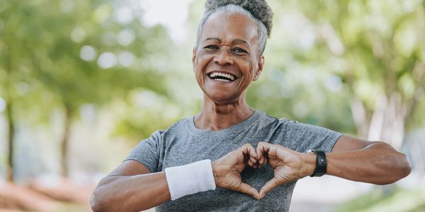Smiling elderly woman making a heart shape with her hands outdoors.