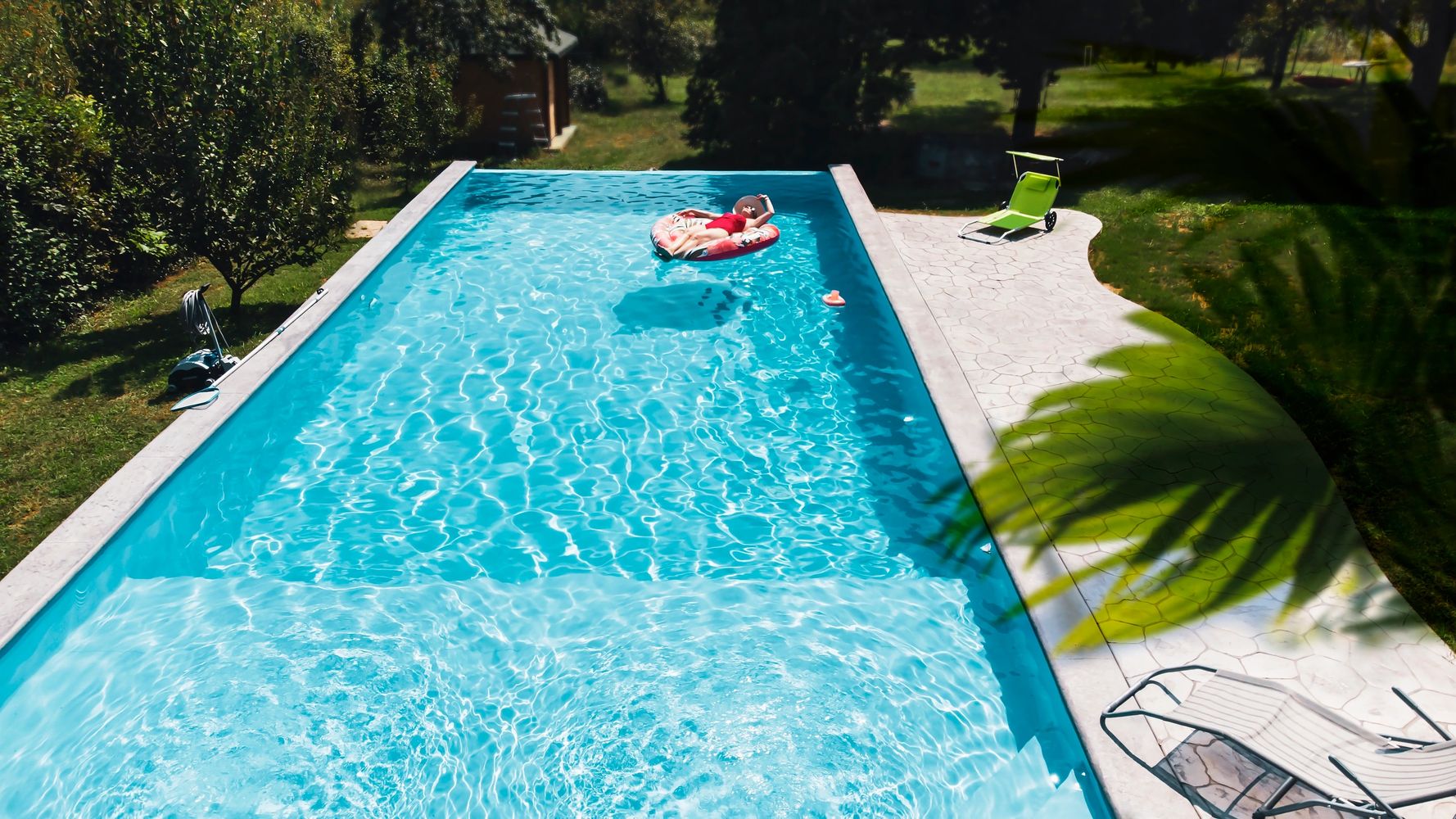 Person relaxing on a float in a sunny backyard pool.