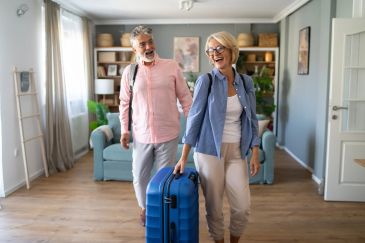 Happy elderly couple arriving home with luggage.