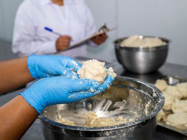Person shaping dough balls wearing blue gloves in a kitchen.