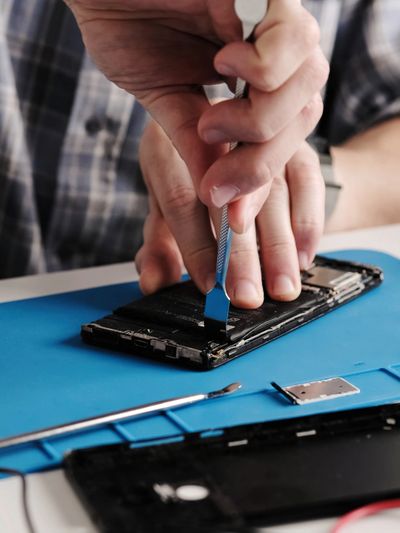 Person repairing a smartphone with tools on a work mat.